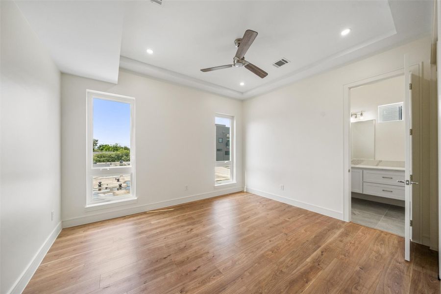 Secondary bedroom with wood floors, recessed lighting, and a ceiling fan. Features large windows for natural light and an ensuite bathroom with modern fixtures.