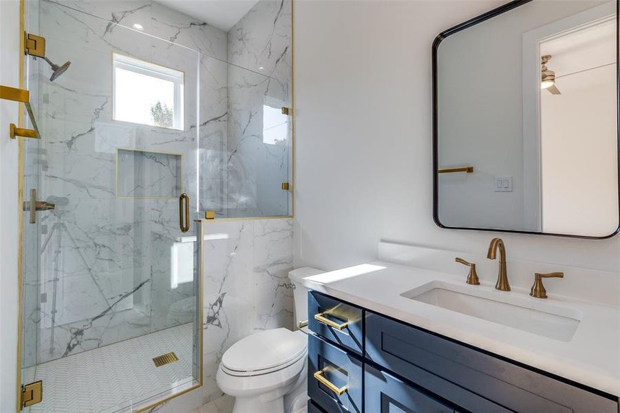 Bathroom with a shower with door, vanity, toilet, and tile walls