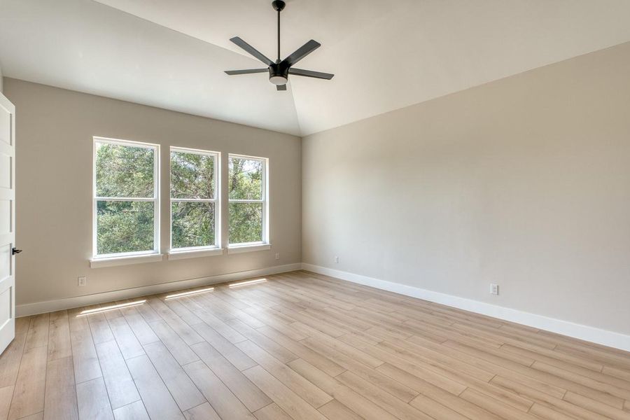 A spacious room offers vaulted ceilings, wood flooring, and ample natural illumination through three large windows.