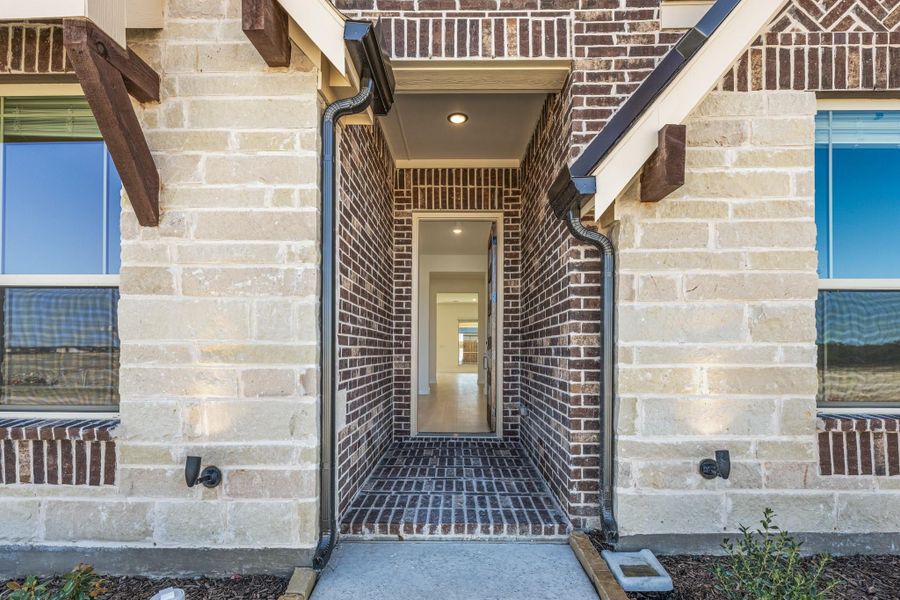 Covered front entry with dark brick archway, stone exterior walls, and open front door leading inside Covered front entry with dark brick archway, stone exterior walls, and open front door leading inside