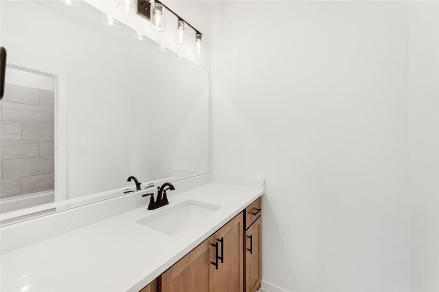 Bathroom vanity with white quartz countertop, wood cabinets, black fixtures, and large mirror with pendant lights above Bathroom vanity with white quartz countertop, wood cabinets, black fixtures, and large mirror with pendant lights above