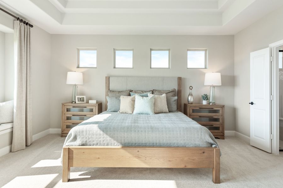 Master bedroom with wood bed frame, tray ceiling, and four small windows above the headboard