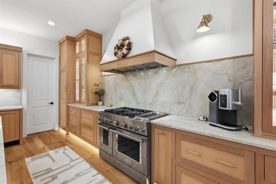 Kitchen featuring range with two ovens, glass fronted cabinets, light stone countertops, light wood-style floors, and tasteful backsplash