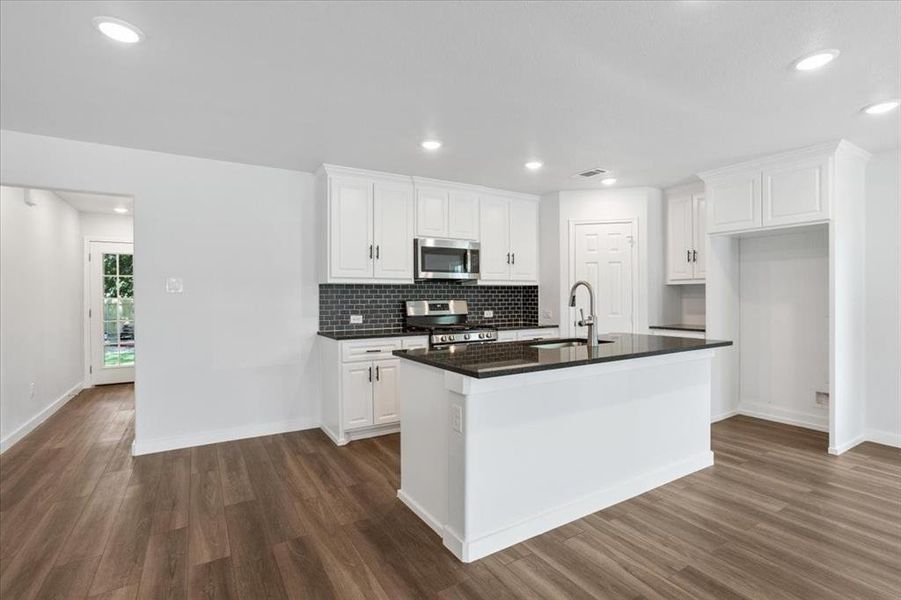 Kitchen featuring stainless steel appliances, dark hardwood / wood-style flooring, and an island with sink