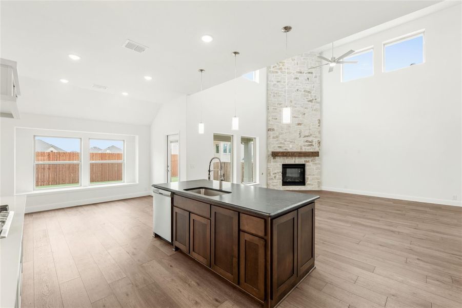 Open-concept kitchen with dark wood island, stone fireplace, vaulted ceiling, and hardwood floors