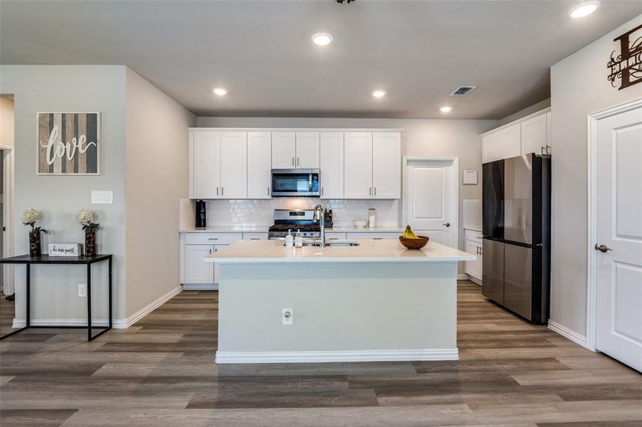 Kitchen featuring stainless steel appliances, white cabinetry, an island with sink, dark wood-style floors, and recessed lighting