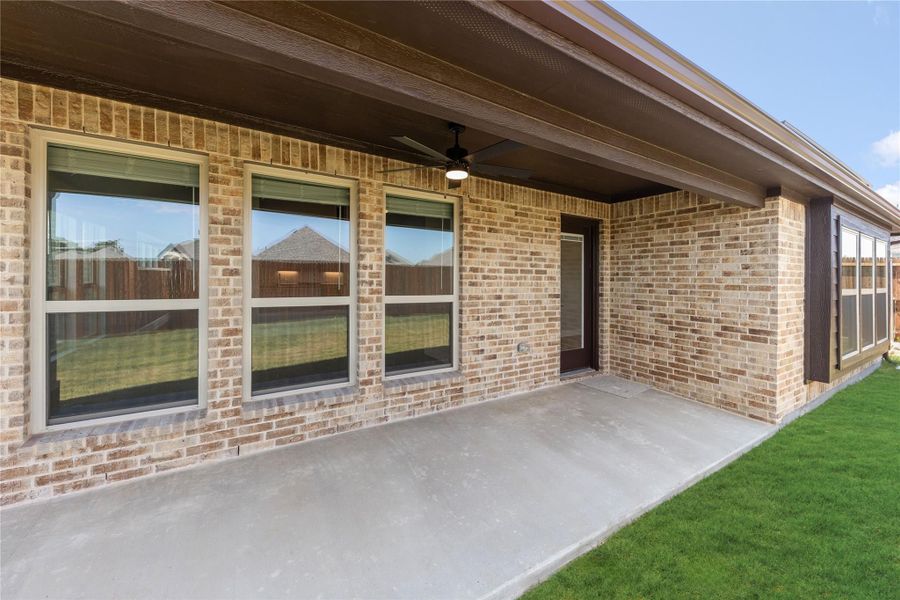 Covered back patio with concrete floor, ceiling fan, brick exterior, and large windows overlooking green lawn Covered back patio with concrete floor, ceiling fan, brick exterior, and large windows overlooking green lawn