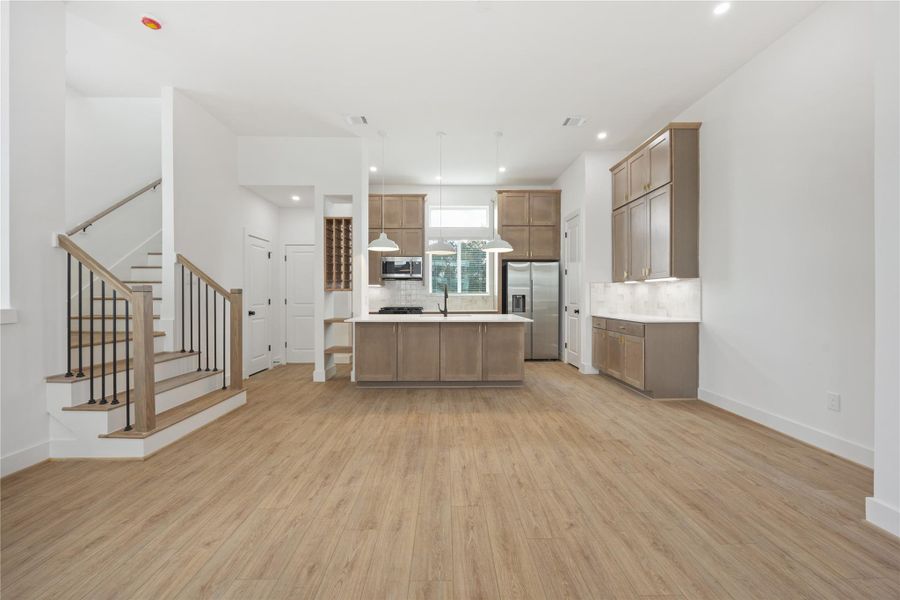 The main living area leads directly to a beautifully finished kitchen with an oversized island, pendant lighting, warm cabinetry, black accents, stainless steel appliances, and a built-in wine/display feature. This open layout is ideal for entertaining, casual dining, and everyday living.