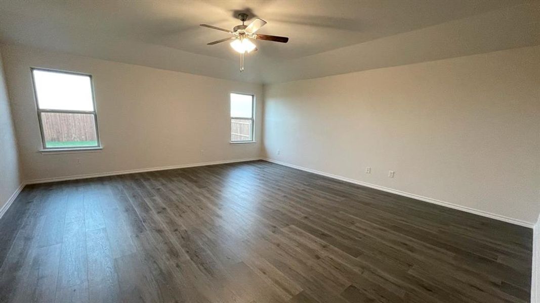 Spacious room featuring wood-finish flooring, light-toned walls, a ceiling fan with integrated lighting, and multiple windows Spacious room featuring wood-finish flooring, light-toned walls, a ceiling fan with integrated lighting, and multiple windows