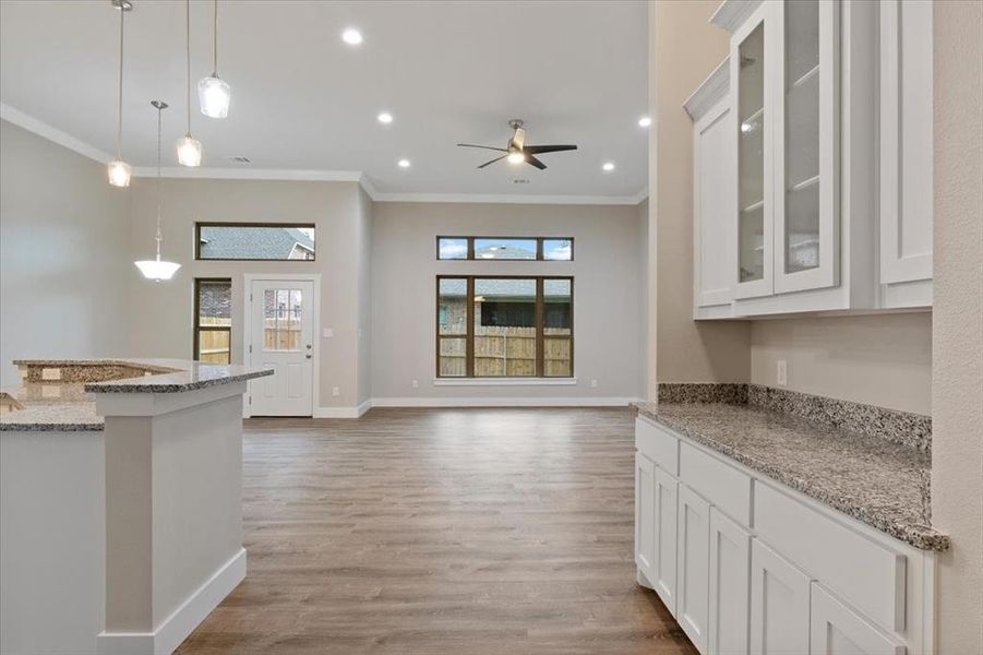 Kitchen with white cabinets, decorative light fixtures, light wood-type flooring, ceiling fan, and ornamental molding