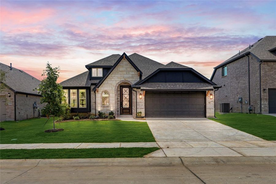 Single-story home with stone exterior, two-car garage, arched entry, and manicured front lawn at dusk