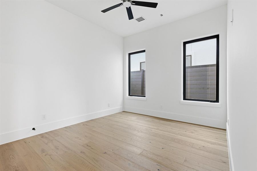 This bright secondary bedroom offers neutral walls, light-toned wood floors, and dual windows for natural light.