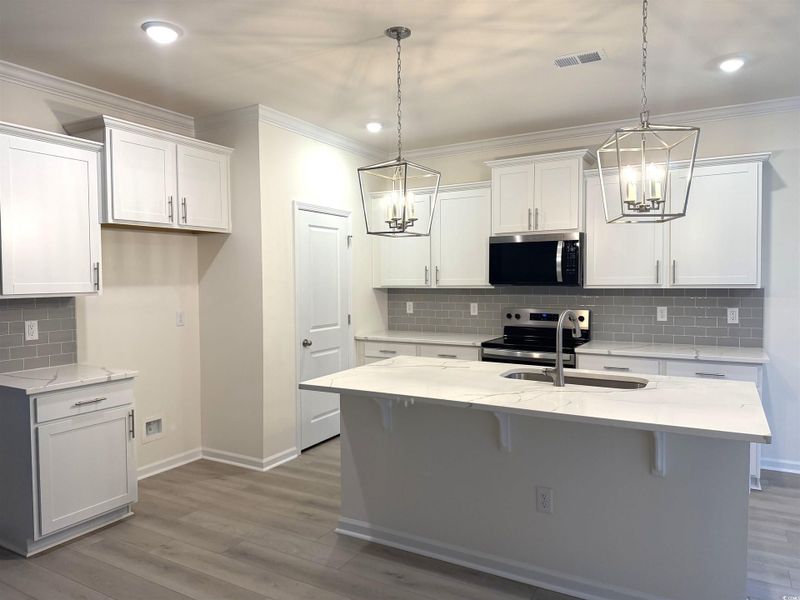 Kitchen with white cabinetry, quartz counters, light wood finished floors, hanging light fixtures, and crown molding