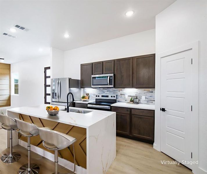 Kitchen with dark wood finish cabinetry, stainless steel appliances, a kitchen breakfast bar, a kitchen island with sink, and light wood-style flooring