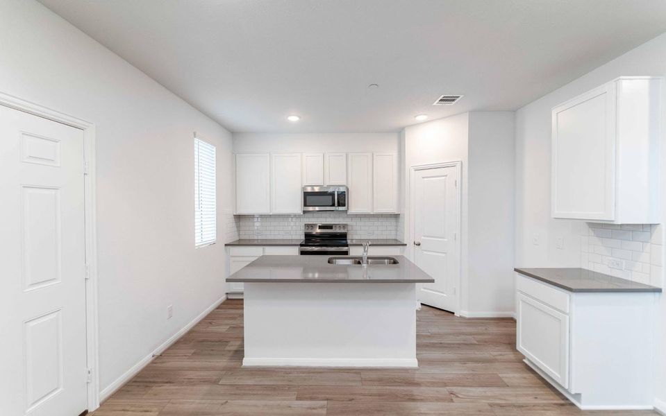 Kitchen featuring white cabinetry, an island with sink, stainless steel appliances, backsplash, and light wood finished floors
