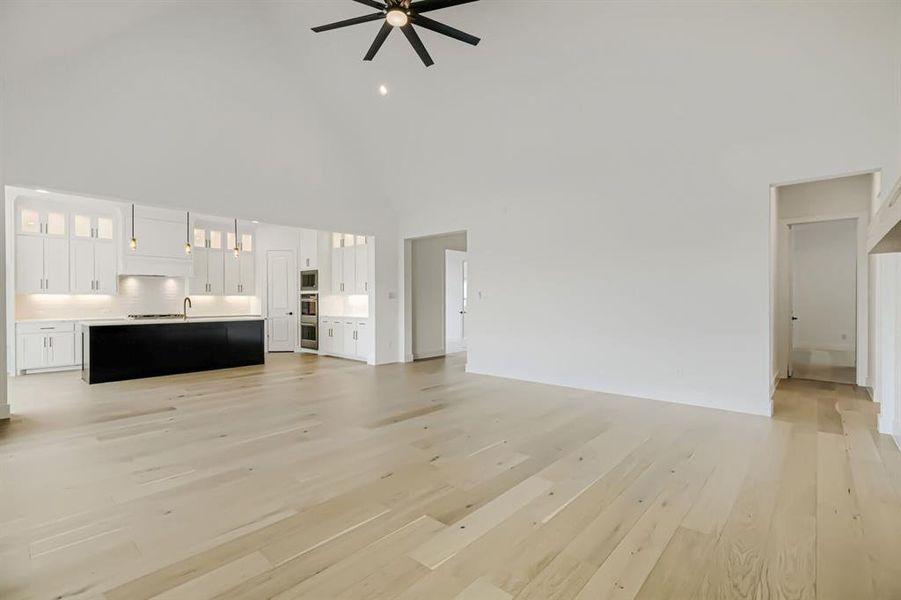Unfurnished living room featuring ceiling fan, light wood-type flooring, and a high ceiling