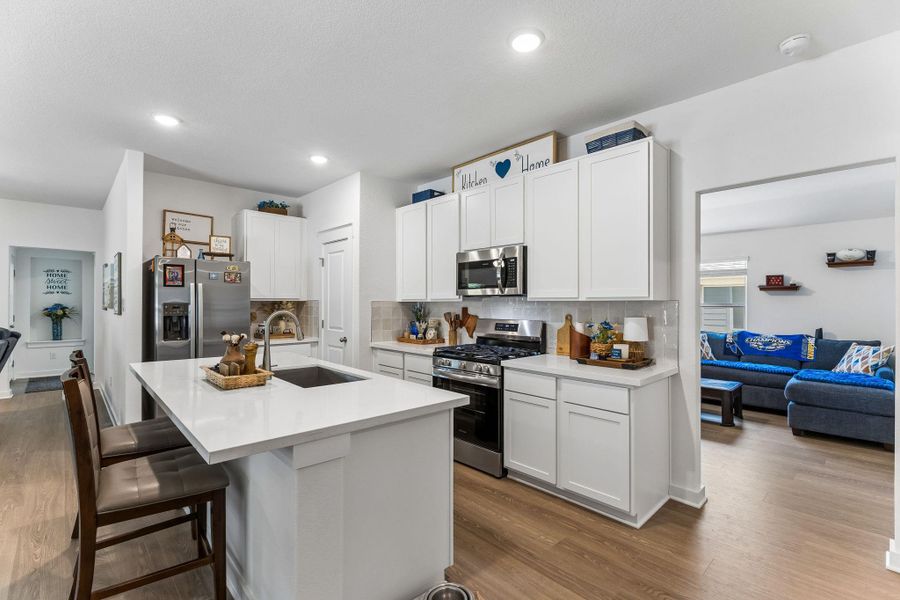 Kitchen featuring white shaker cabinetry, quartz countertops, stainless steel appliances, a gas range, and wood-finish flooring