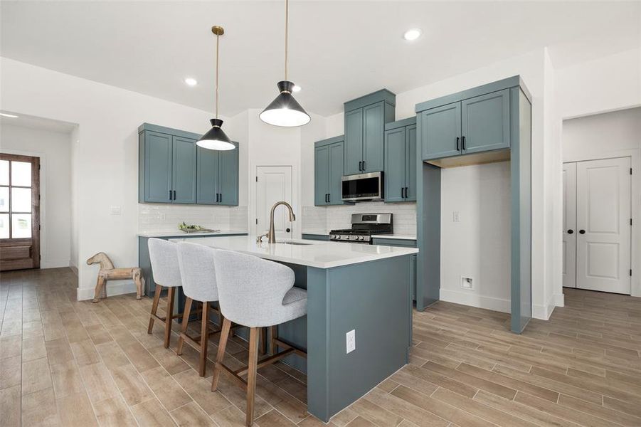 Kitchen featuring hanging light fixtures, appliances with stainless steel finishes, tasteful backsplash, and a kitchen island with sink