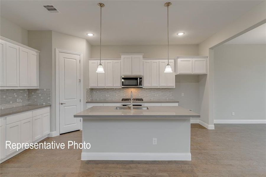 Kitchen with white cabinetry, light hardwood / wood-style floors, and an island with sink