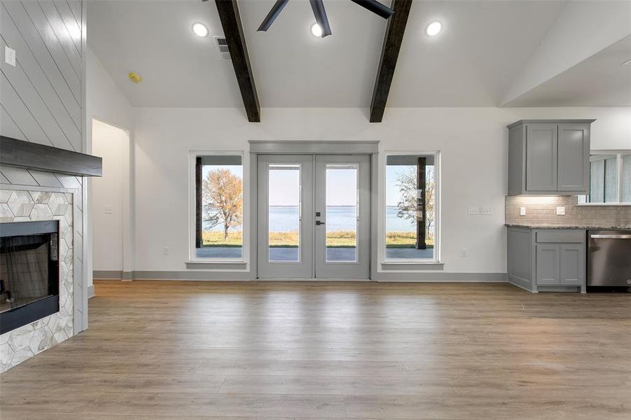 Unfurnished living room with beamed ceiling, light hardwood / wood-style floors, a stone fireplace, and plenty of natural light