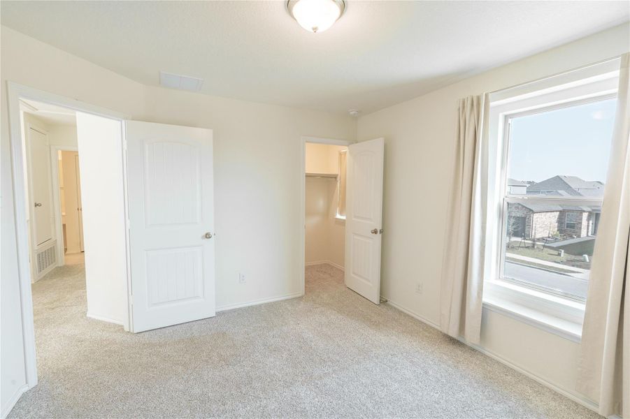 A well-lit bedroom features plush carpeting and a large window offering neighborhood views. A well-lit bedroom features plush carpeting and a large window offering neighborhood views.