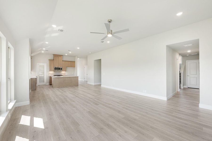 Open living area with light wood floors, ceiling fan, and kitchen with island in background