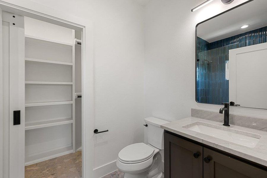 Modern bathroom featuring a sleek vanity with stone counters and a spacious built-in closet.