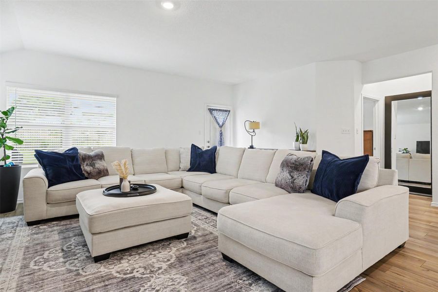 Spacious living area featuring high vaulted ceilings, recessed lighting, wood-finish flooring, and a large window with horizontal blinds