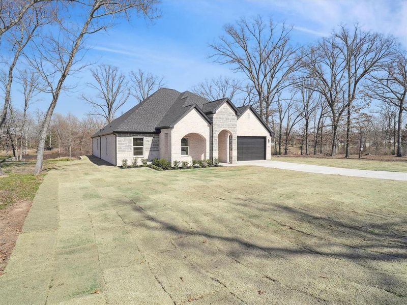 French provincial home with driveway, stone siding, a garage, a front yard, and a shingled roof