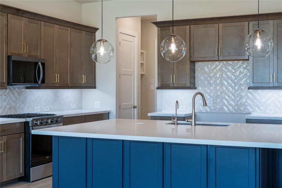 The kitchen is more than just a place to cook; it's a central gathering space designed for creating memories, entertaining guests, and daily living. This beautiful kitchen island has an extended breakfast bar and is painted in a gorgeous navy color with quartz countertop, and pendant lighting.