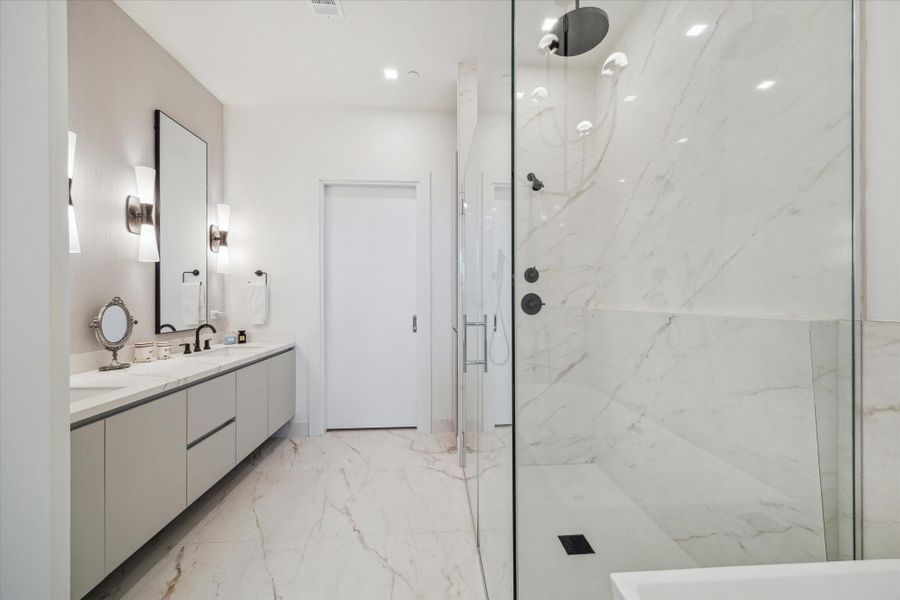 Primary bath with curbless shower, soaking tub, wallcovering, designer lighting and mirrors.  Door leads to primary closet.
