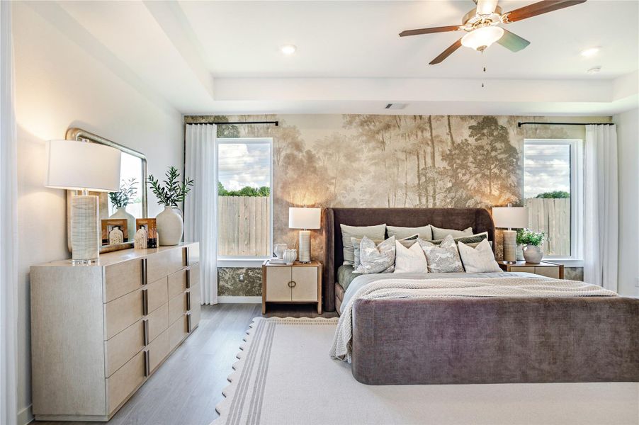 The Primary bedroom features a modern design with a large upholstered bed, neutral tones, and a nature-themed accent wall. It includes two windows for natural light, a ceiling fan, and ample storage with a stylish dresser and nightstands. The Primary bedroom features a modern design with a large upholstered bed, neutral tones, and a nature-themed accent wall. It includes two windows for natural light, a ceiling fan, and ample storage with a stylish dresser and nightstands.