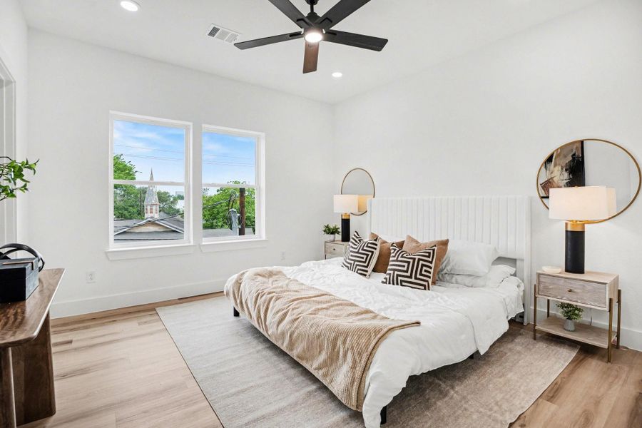 Bright and modern primary bedroom with large windows, wood flooring, and a ceiling fan, creating an inviting atmosphere.