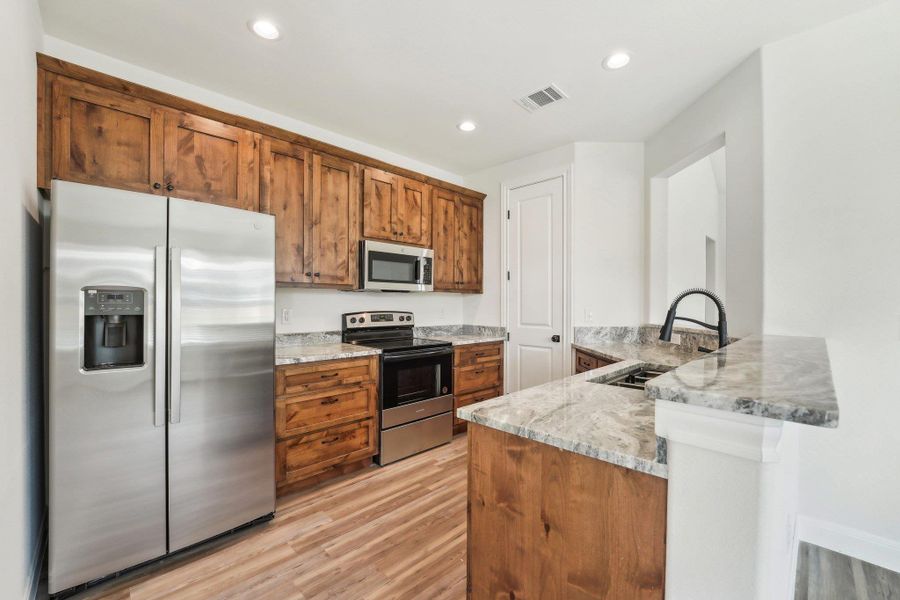 Kitchen featuring a peninsula, appliances with stainless steel finishes, visible vents, and wood-style vinyl flooring Kitchen featuring a peninsula, appliances with stainless steel finishes, visible vents, and wood-style vinyl flooring