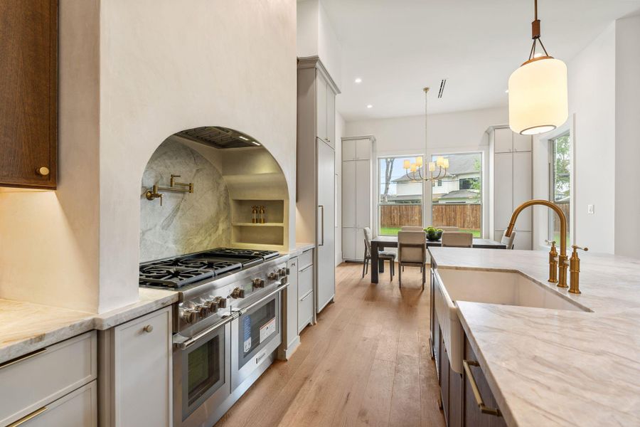 A beautifully designed cooking space is framed by a custom arched niche with a full-height stone backsplash. Professional-grade appliances and integrated storage create a functional yet refined culinary environment.