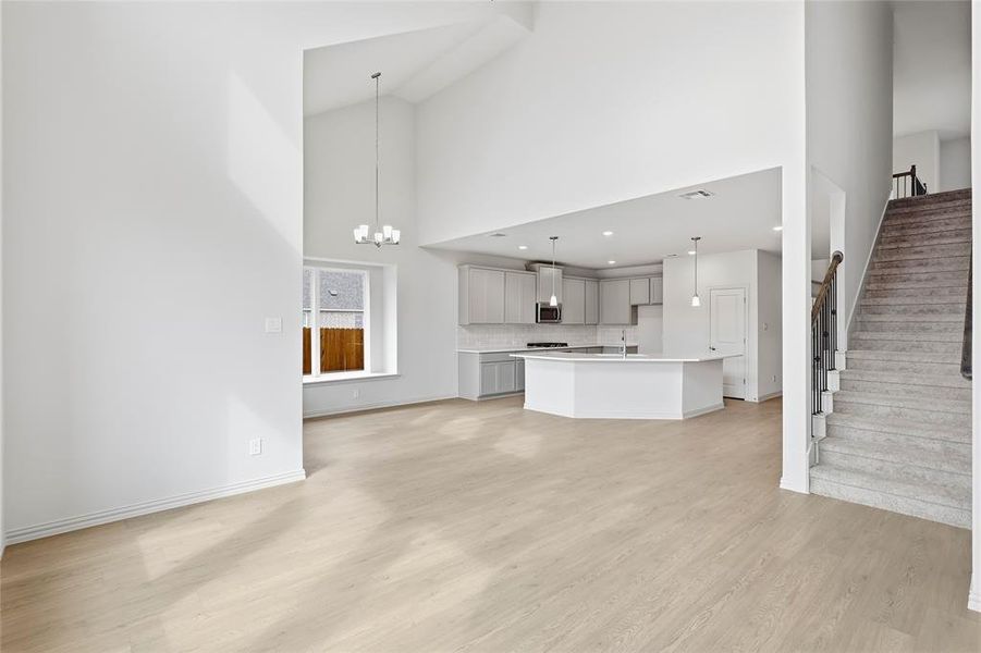 Unfurnished living room with suspended lighting, light wood-style flooring, and vaulted ceiling