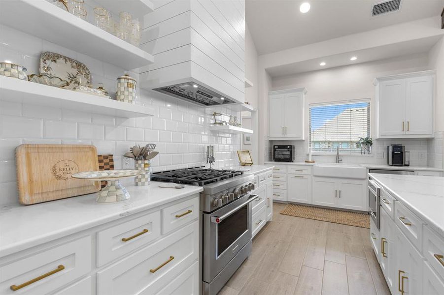 Kitchen with open shelves, white cabinetry, stainless steel appliances, tasteful backsplash, and custom range hood Kitchen with open shelves, white cabinetry, stainless steel appliances, tasteful backsplash, and custom range hood