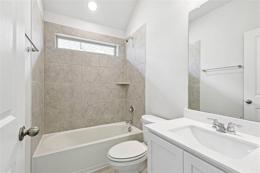 Full bathroom featuring vanity, tiled shower / bath combo, toilet, and vaulted ceiling