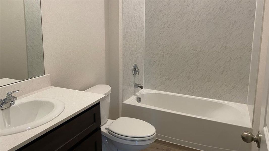 Full bath with vanity, a textured wall,  shower combination, and dark wood-style flooring