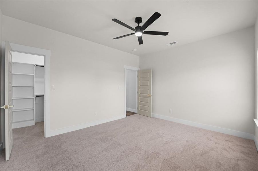 Spacious room featuring neutral carpeting, a contemporary ceiling fan with integrated lighting, and a walk-in closet with built-in shelving Spacious room featuring neutral carpeting, a contemporary ceiling fan with integrated lighting, and a walk-in closet with built-in shelving