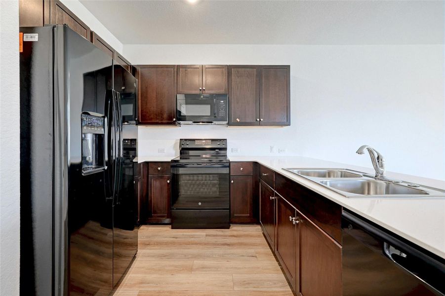 Kitchen featuring black appliances, dark wood finish cabinets, light countertops, light wood-style flooring, and a peninsula