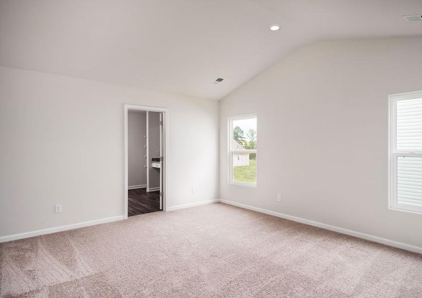 Master bedroom with two windows, tan walls and carpet.