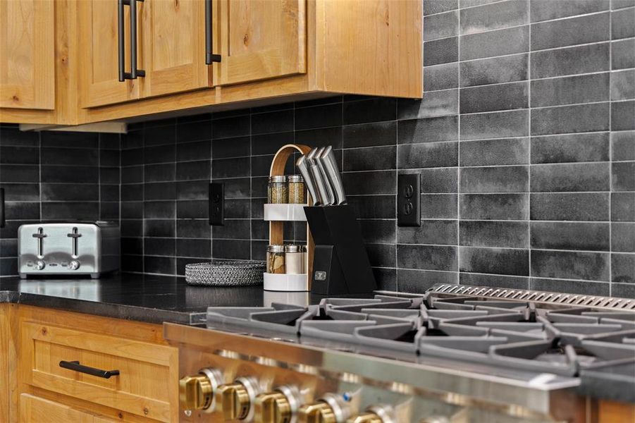 Kitchen featuring light wood finish cabinetry, backsplash, and stainless steel gas range oven