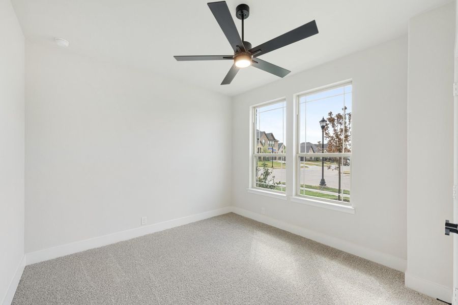 Empty bedroom with carpet flooring, black ceiling fan, and two windows overlooking a neighborhood street