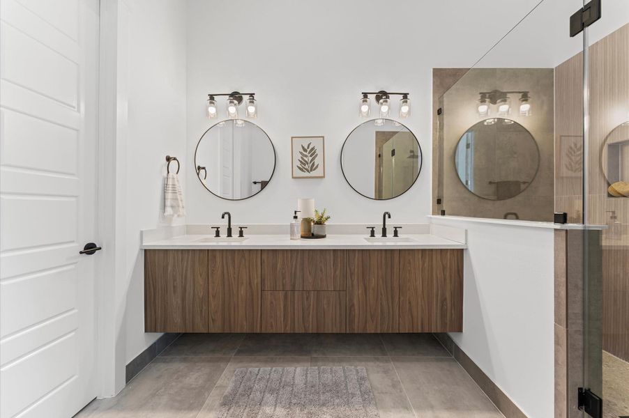The luxurious primary ensuite features sleek modern finishes, a glass-enclosed shower with stylish tile, and a double-sink vanity topped with quartz countertops, complemented by two contemporary mirrors and lighting fixtures, creating a bright, elegant, and functional retreat.