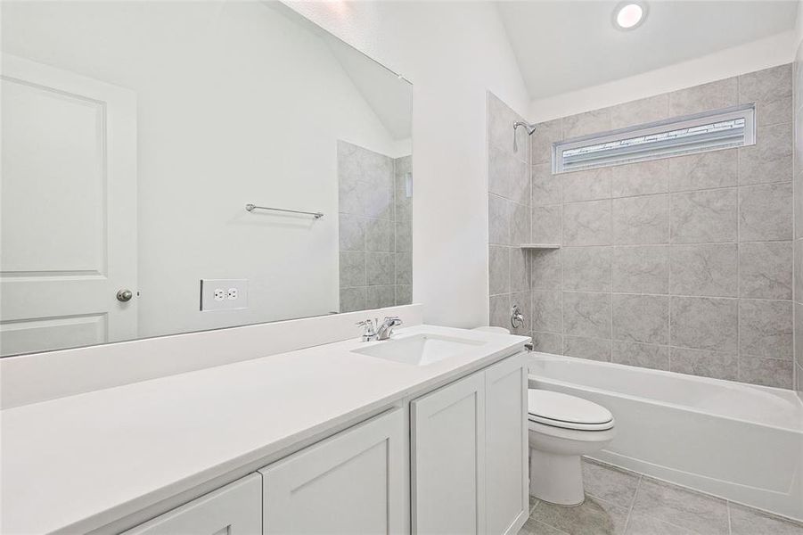 Full bathroom with vanity, lofted ceiling, tiled shower / bath combo, tile patterned floors, and toilet