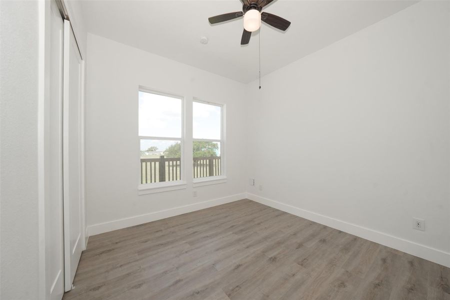 Bright and airy bedroom with large windows, light wood flooring, and a ceiling fan. Ideal for natural light and comfort.