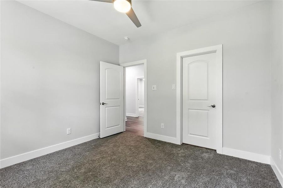 Unfurnished bedroom with dark carpet and a ceiling fan
