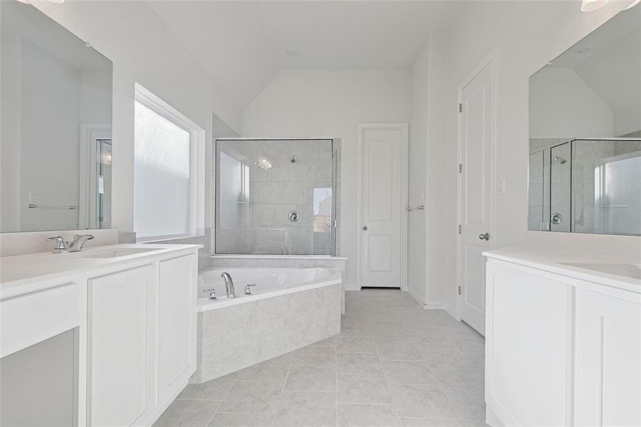 Full bath featuring a shower stall, two vanities, a garden tub, lofted ceiling, and light tile patterned floors Full bath featuring a shower stall, two vanities, a garden tub, lofted ceiling, and light tile patterned floors