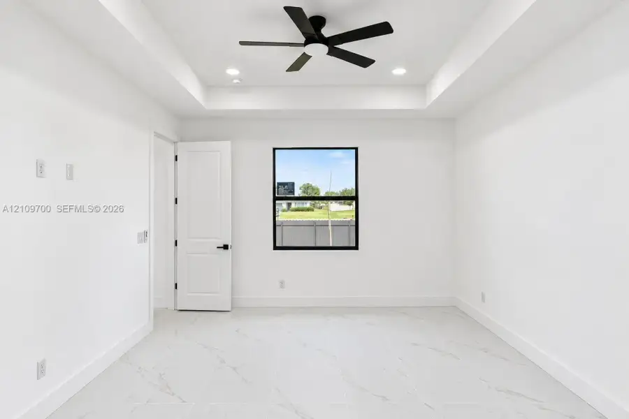 Interior space featuring a recessed tray ceiling, large-format tile flooring with marble-finish veining, a matte black ceiling fan, and black-framed window casing
